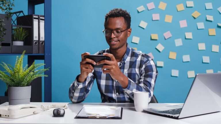 African american businessman playing games on mobile smartphone while in modern workspace office. marketing company financial advisor winning game on mobile device while at work.