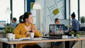 Startup office employee using laptop in video conference with clients and manager talking about marketing strategy. casual business woman in group call discussing with remote coworkers about charts.