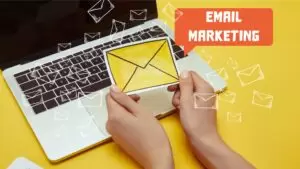 cropped image of woman holding envelope sign near laptop with"email marketing" lettering and email